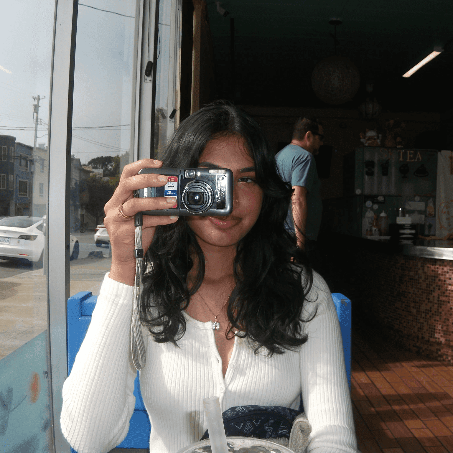 Deepa taking a photo with a compact camera in a café window