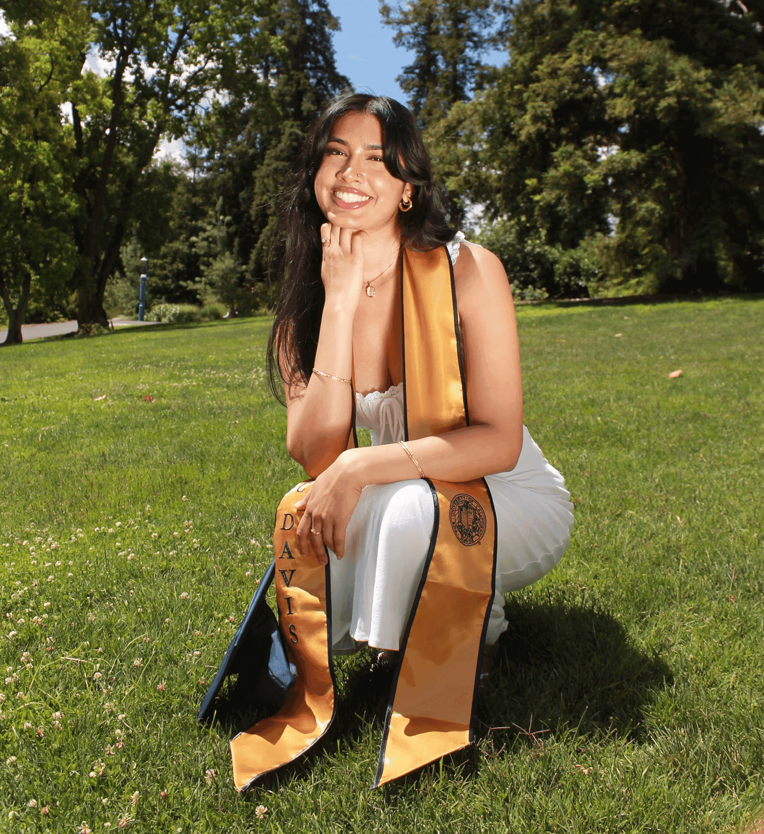 Deepa smiling in a grassy park, wearing a graduation stole